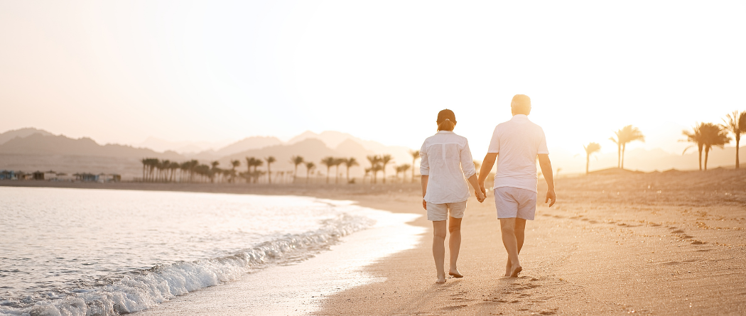 elderly couple walking on beach at sunset