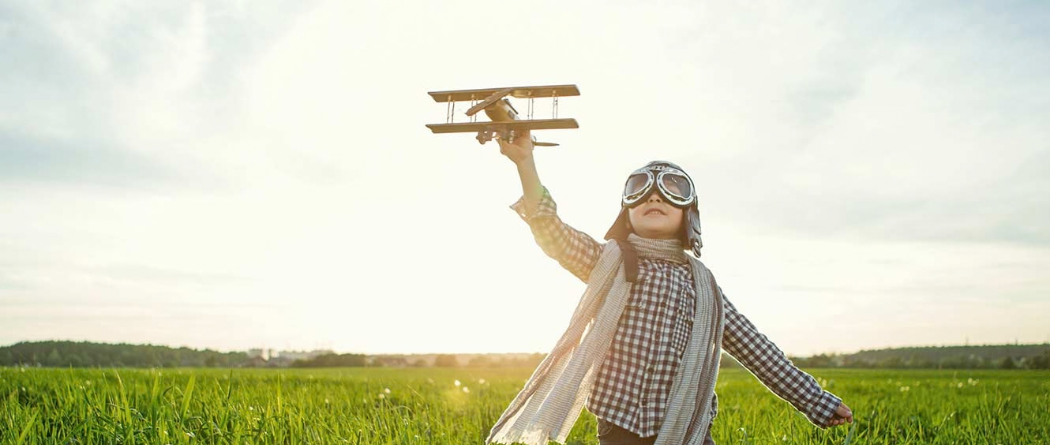 young boy playing with an airplane in a field